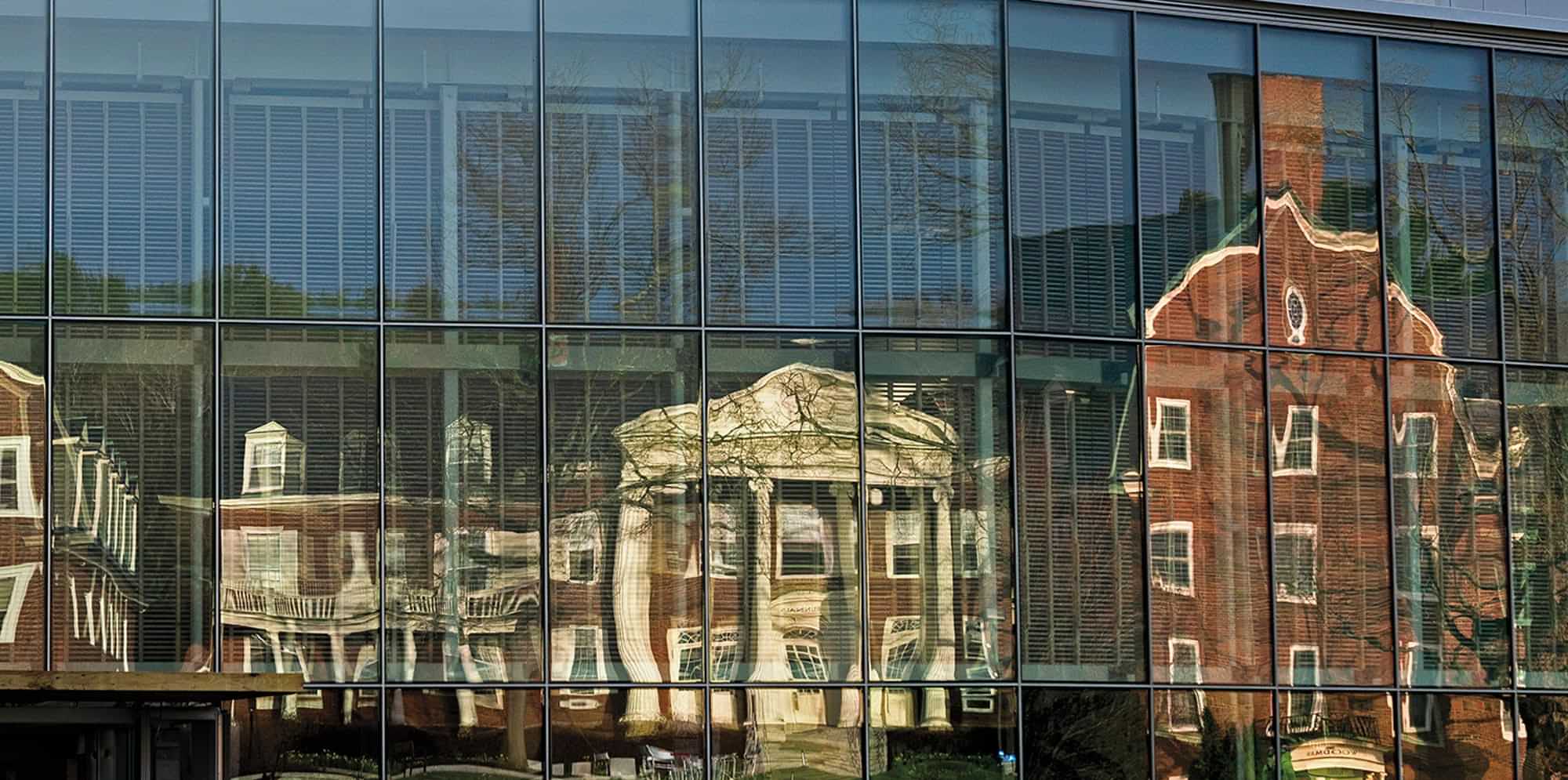 the windows of the Gordon Center for Creative and Performing Arts reflect other older buildings on the Colby campus