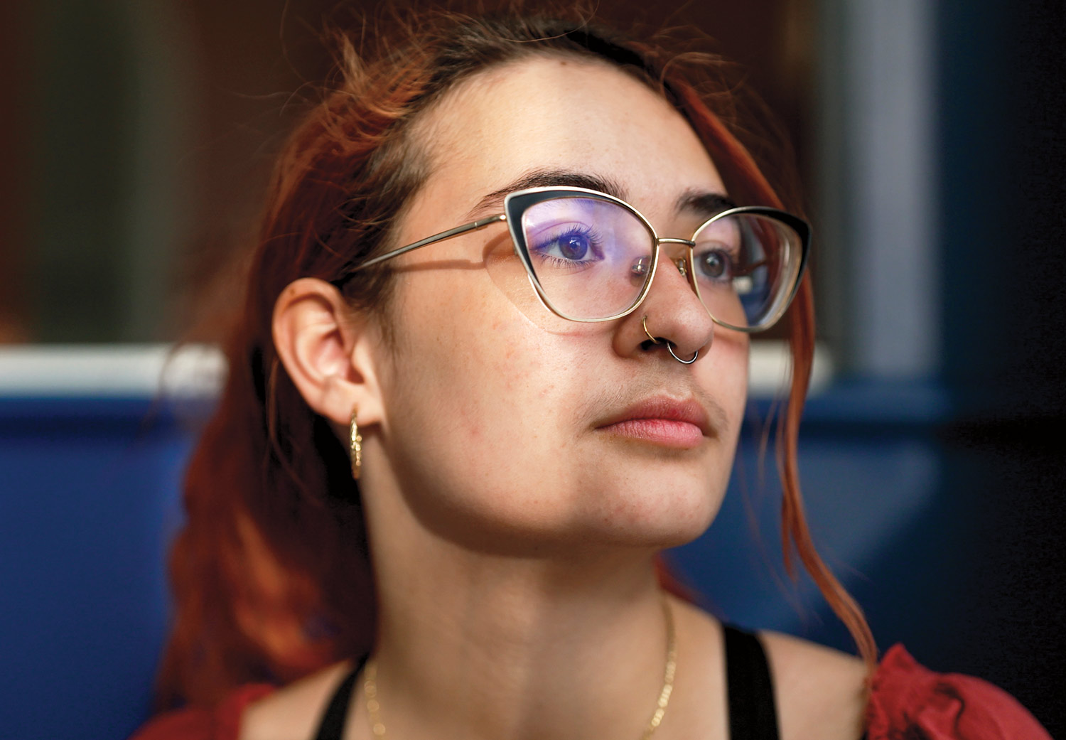 close view of Jay Talmadge ’25 with their orange dyed hair in a loose ponytail and wearing cat-eye frame glasses