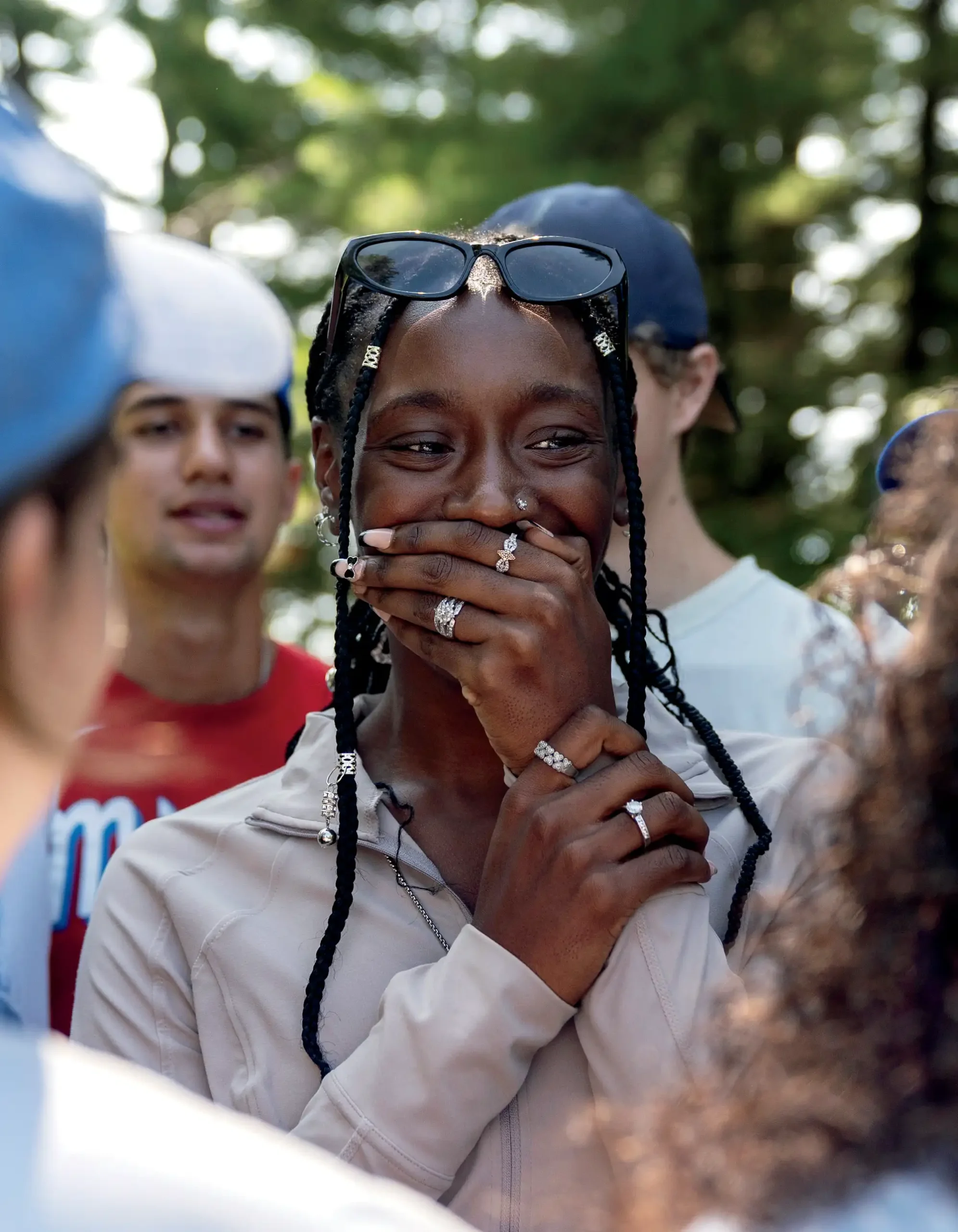 Tori White hiding her smile with her hand while wearing sunglasses and a pink athletic jacket and surrounded by other hikers