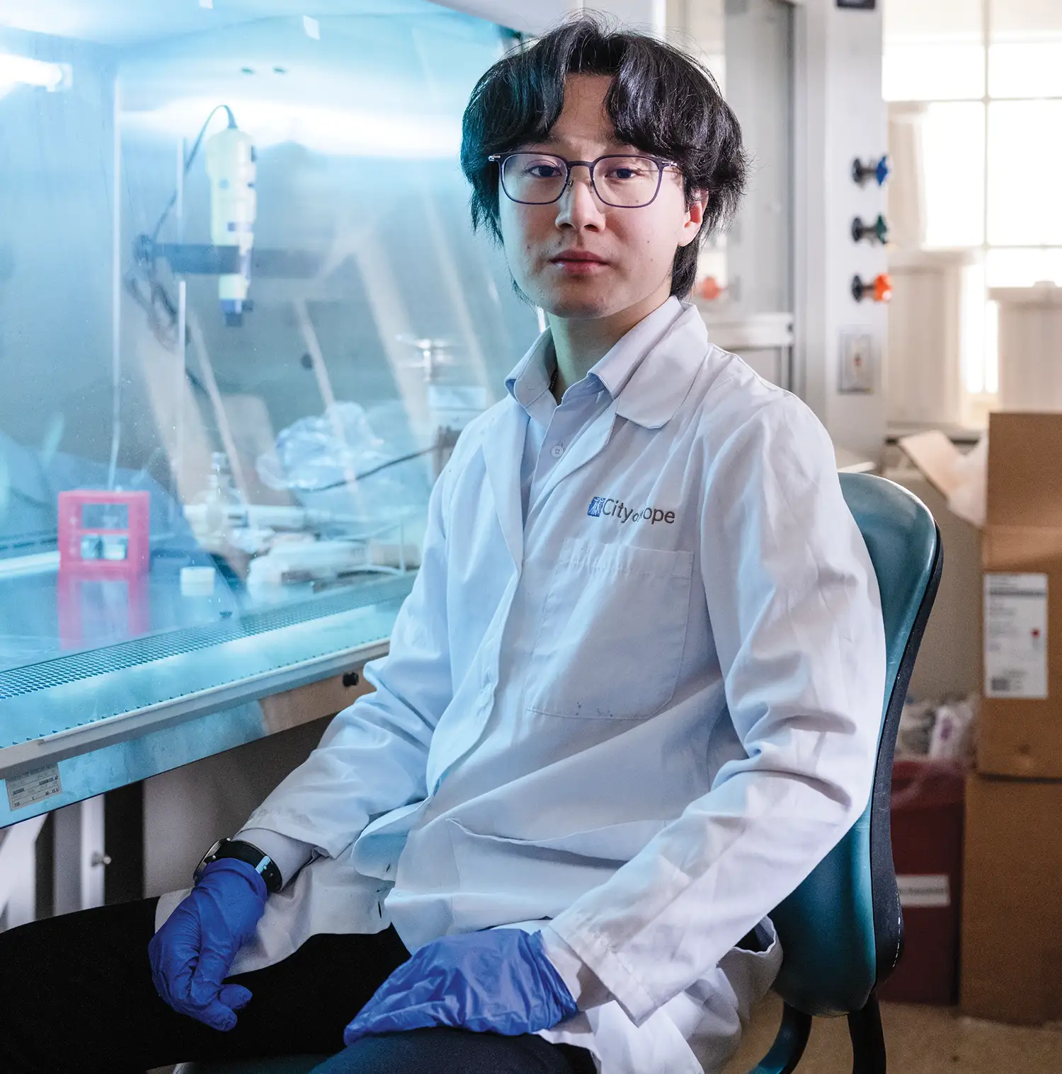 Dimitri Lin wearing a white lab coat and Nitrile gloves while sitting in a lab