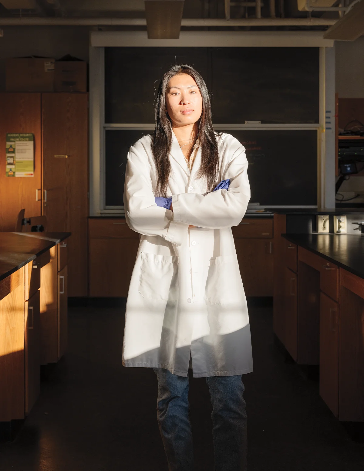 Lily Moy wearing a white lab coat and posing with her arms crossed in a lab