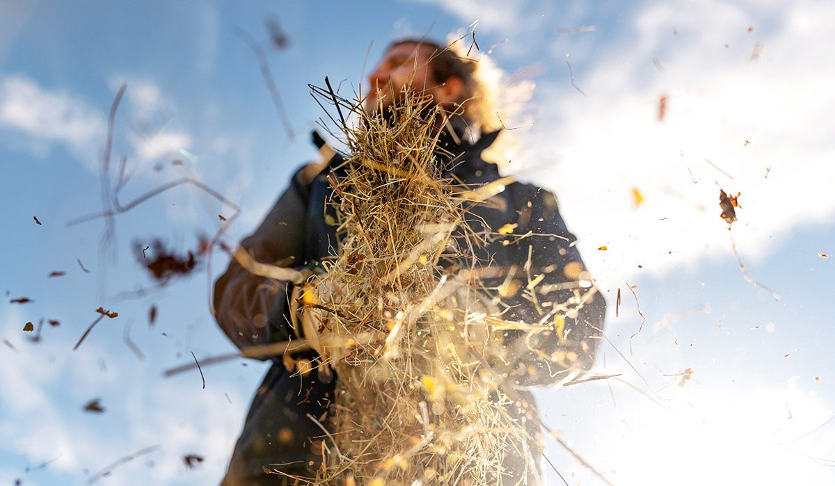 A dramatic, low-angle shot looking up at a person holding a large bunch of dried hay or straw