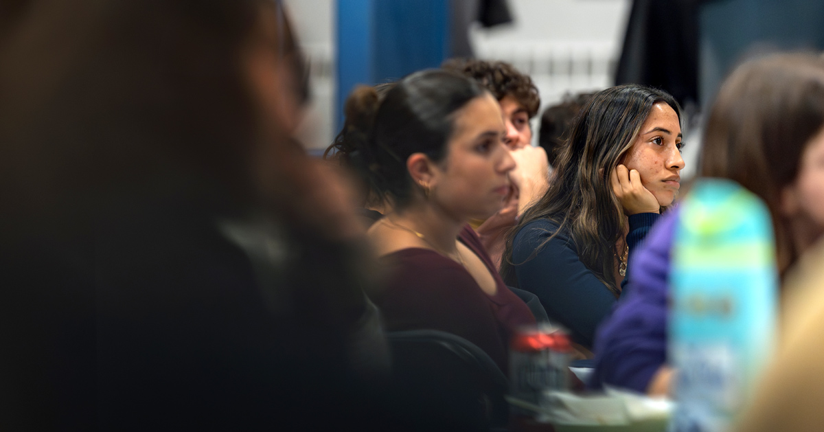 Students sit in an auditorium, listening intently to a panel presentation.