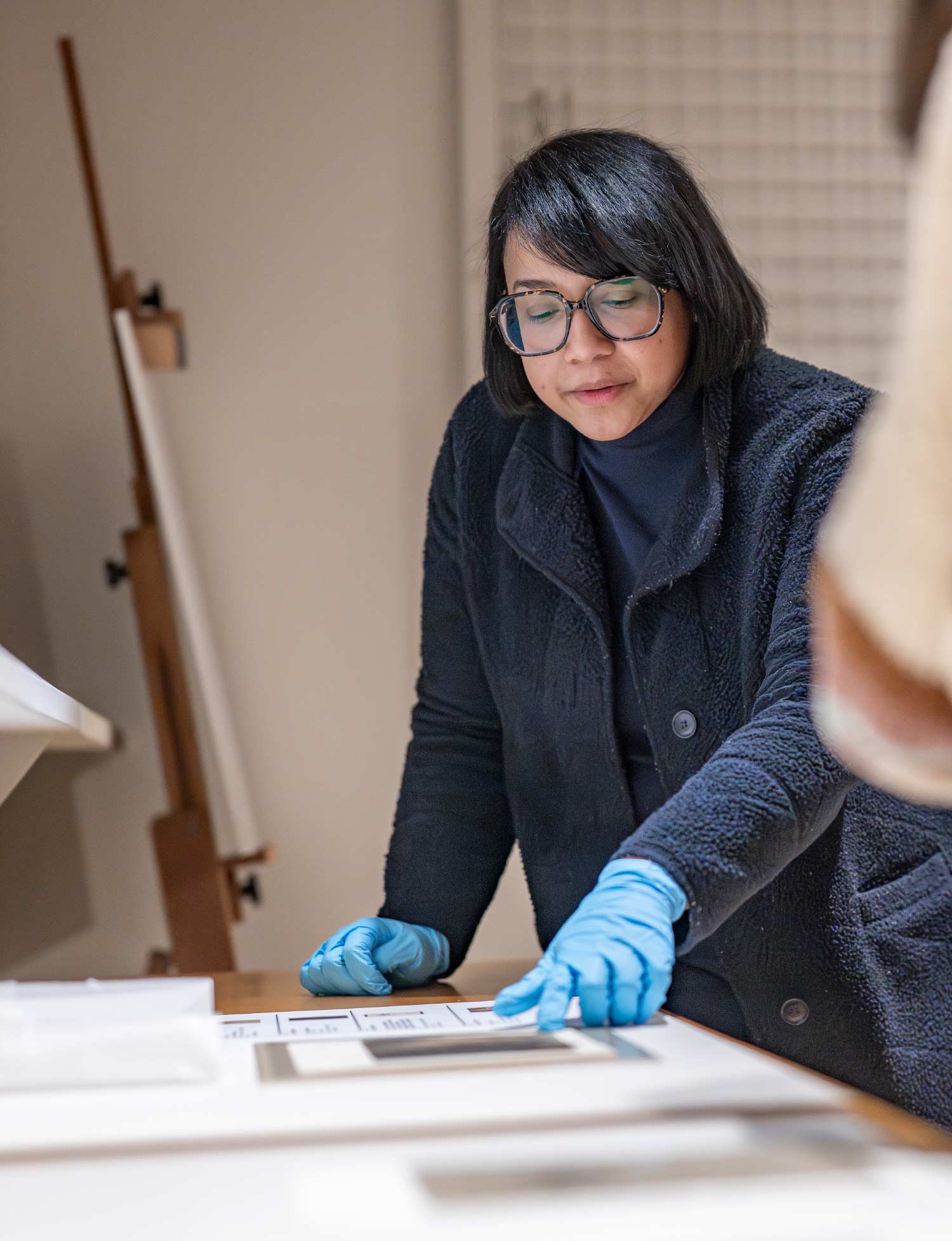 An archivist wearing glasses and blue protective gloves carefully inspects historic documents resting on a clean white surface.
