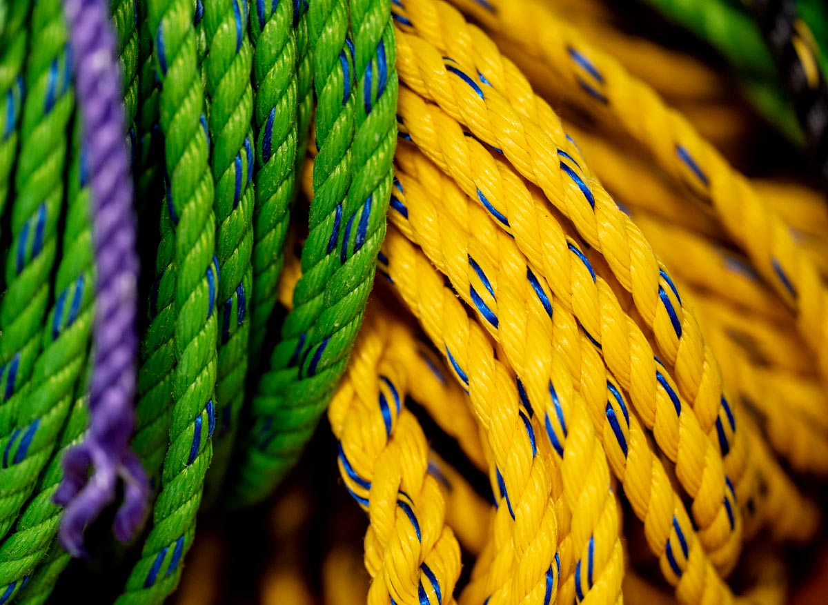 A close-up, detailed view of coiled brightly colored ropes in green and yellow with blue tracer threads, along with a strand of purple rope.